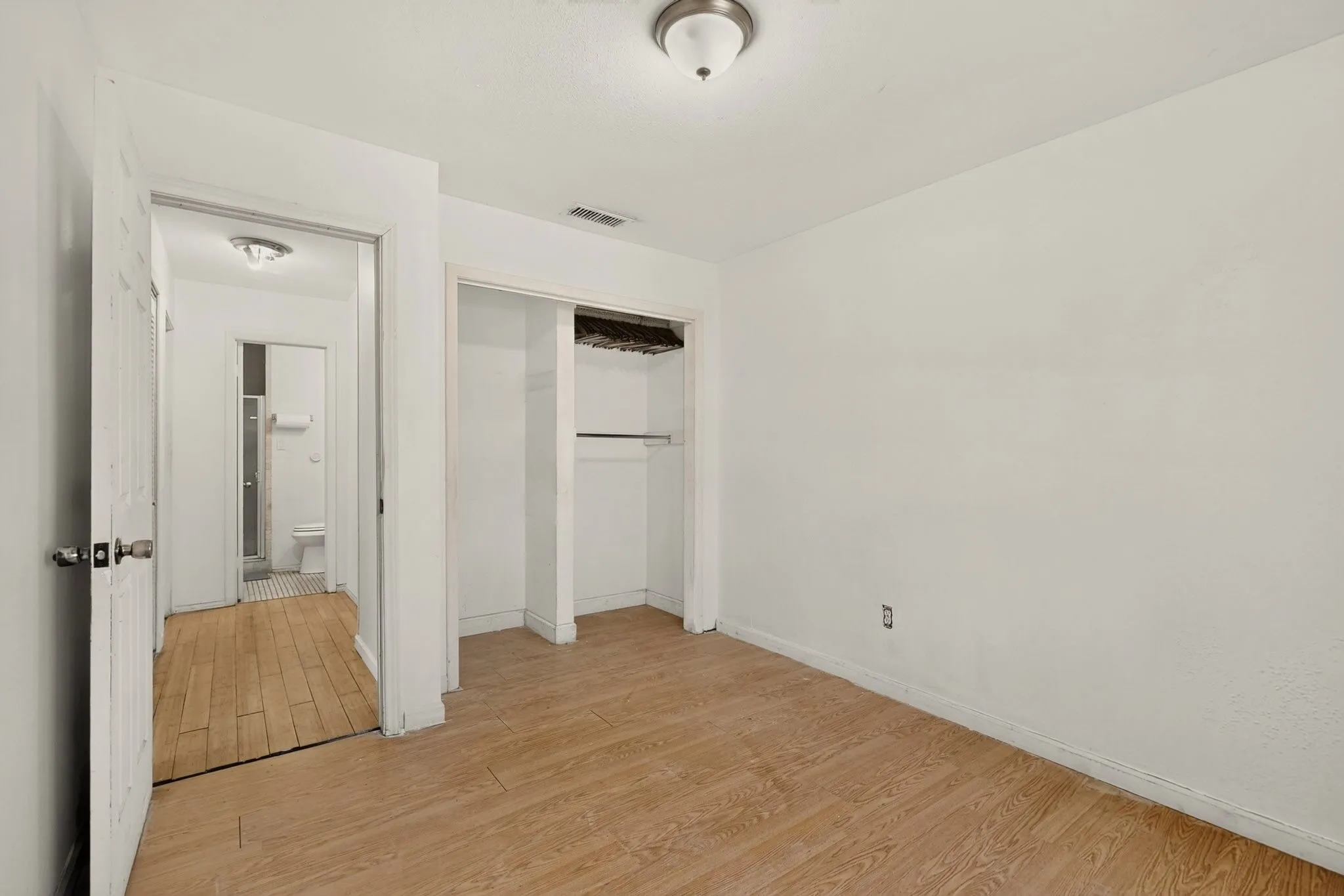Wood-finish flooring, recessed closet with shelving, overhead flush-mount lighting, and white interior doors