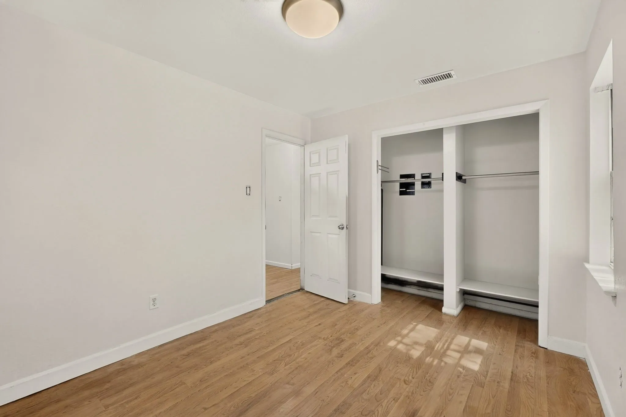 Wood-finish flooring, recessed closet storage, white trim, and a ceiling-mounted light fixture