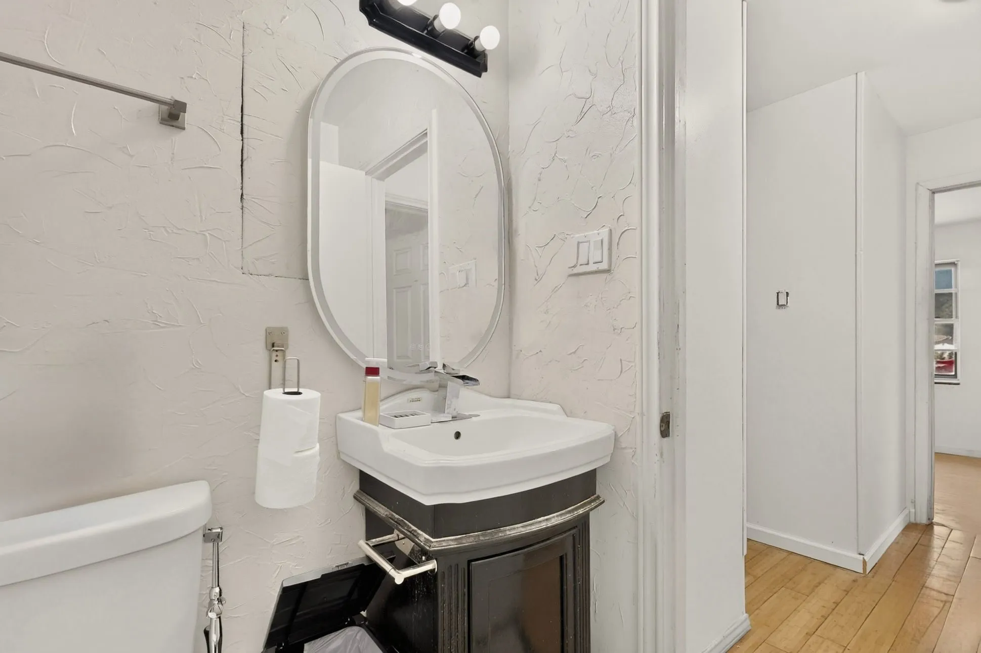 Bathroom featuring an oval mirror, wall-mounted light fixture, pedestal sink, and wood-finish flooring