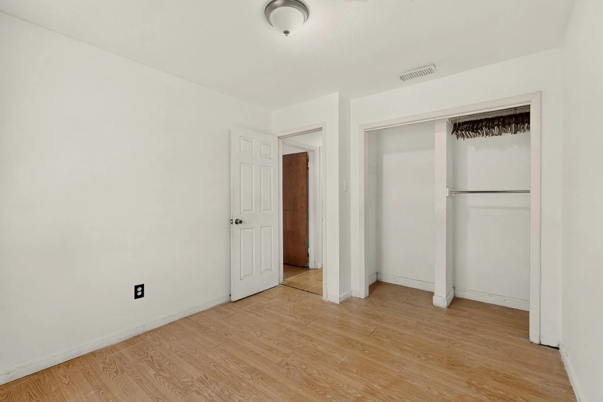 Wood-finish flooring with white baseboards, a white paneled door, and a built-in closet with a hanging rod