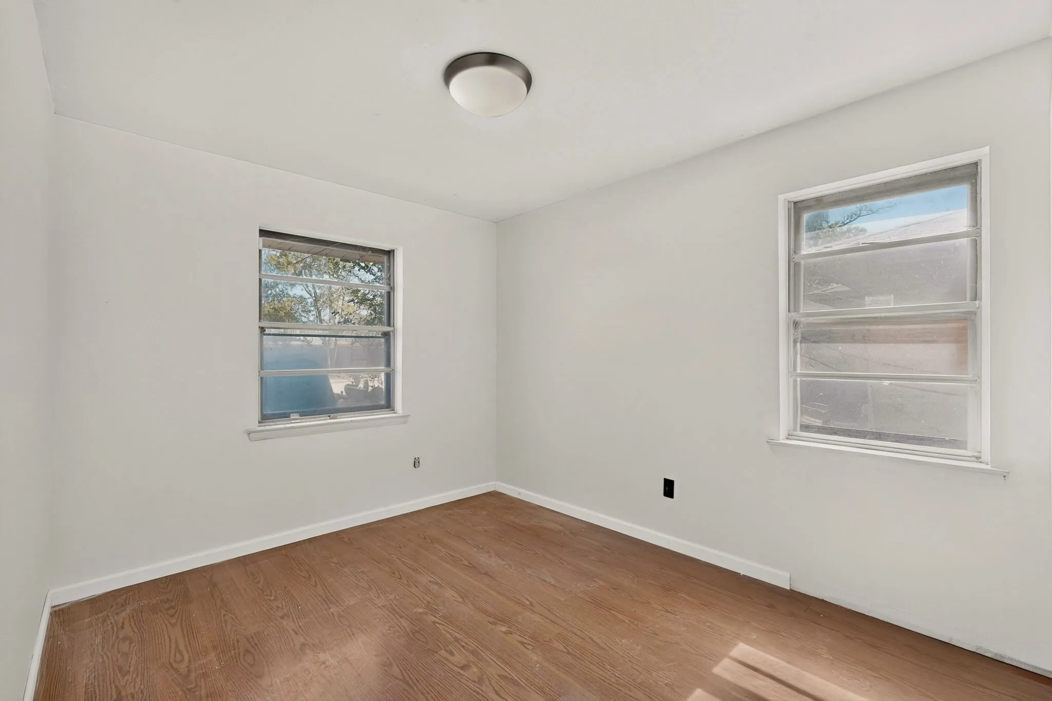Wood-finish flooring, white painted walls, two windows, and a flush-mount ceiling light
