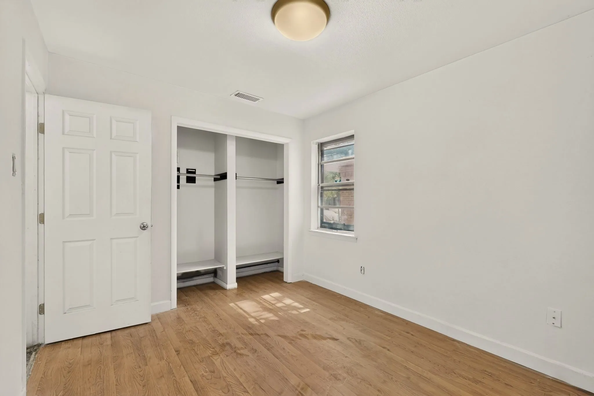 Wood-finish flooring, white walls, built-in closet storage, window with exterior light, and a ceiling-mounted light fixture