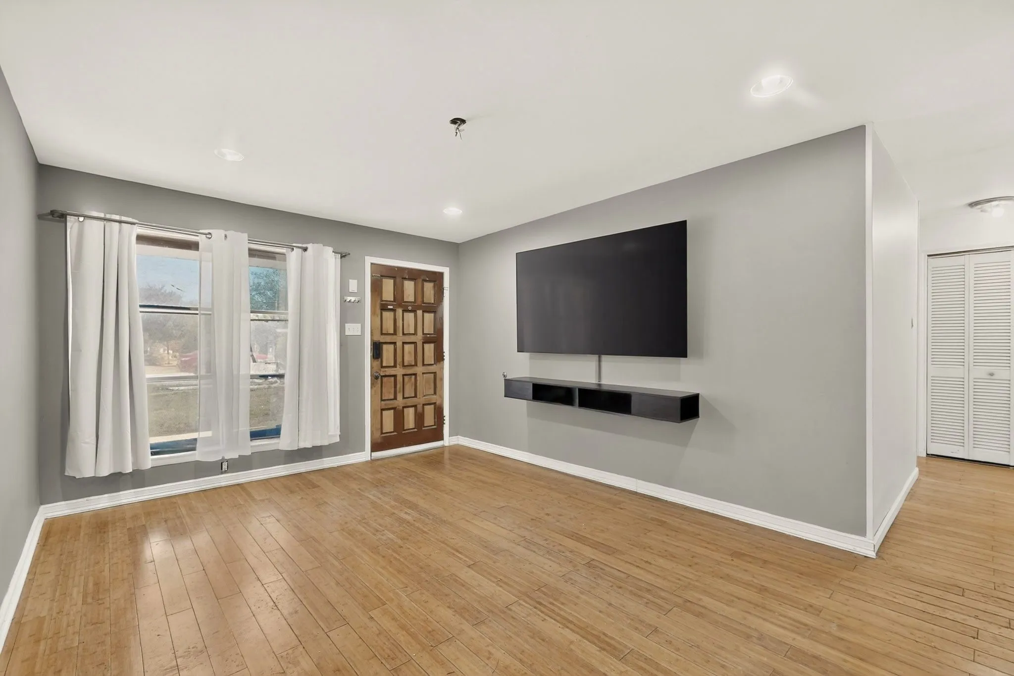 Hardwood flooring, recessed lighting, front entry door with decorative panels, wall-mounted media console, and louvered bifold doors