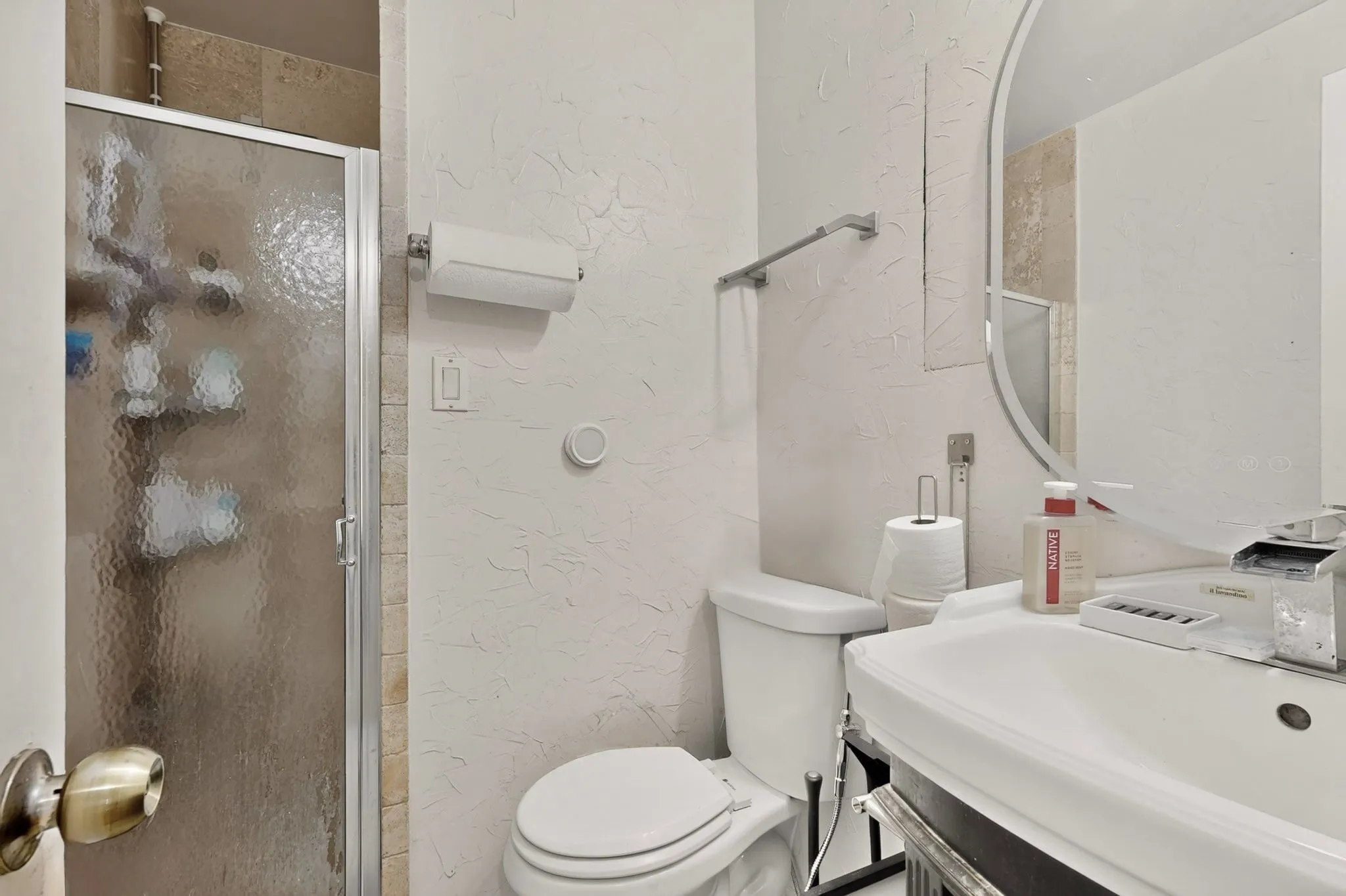 Walk-in shower with frosted glass enclosure, ceramic tile surround, pedestal sink, and wall-mounted mirror