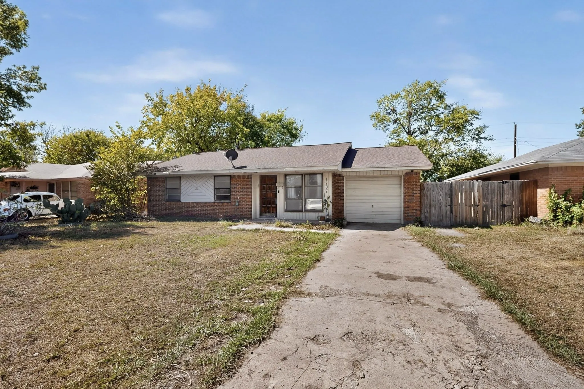 Brick exterior, attached garage, paved driveway, shingle roof, and mature trees