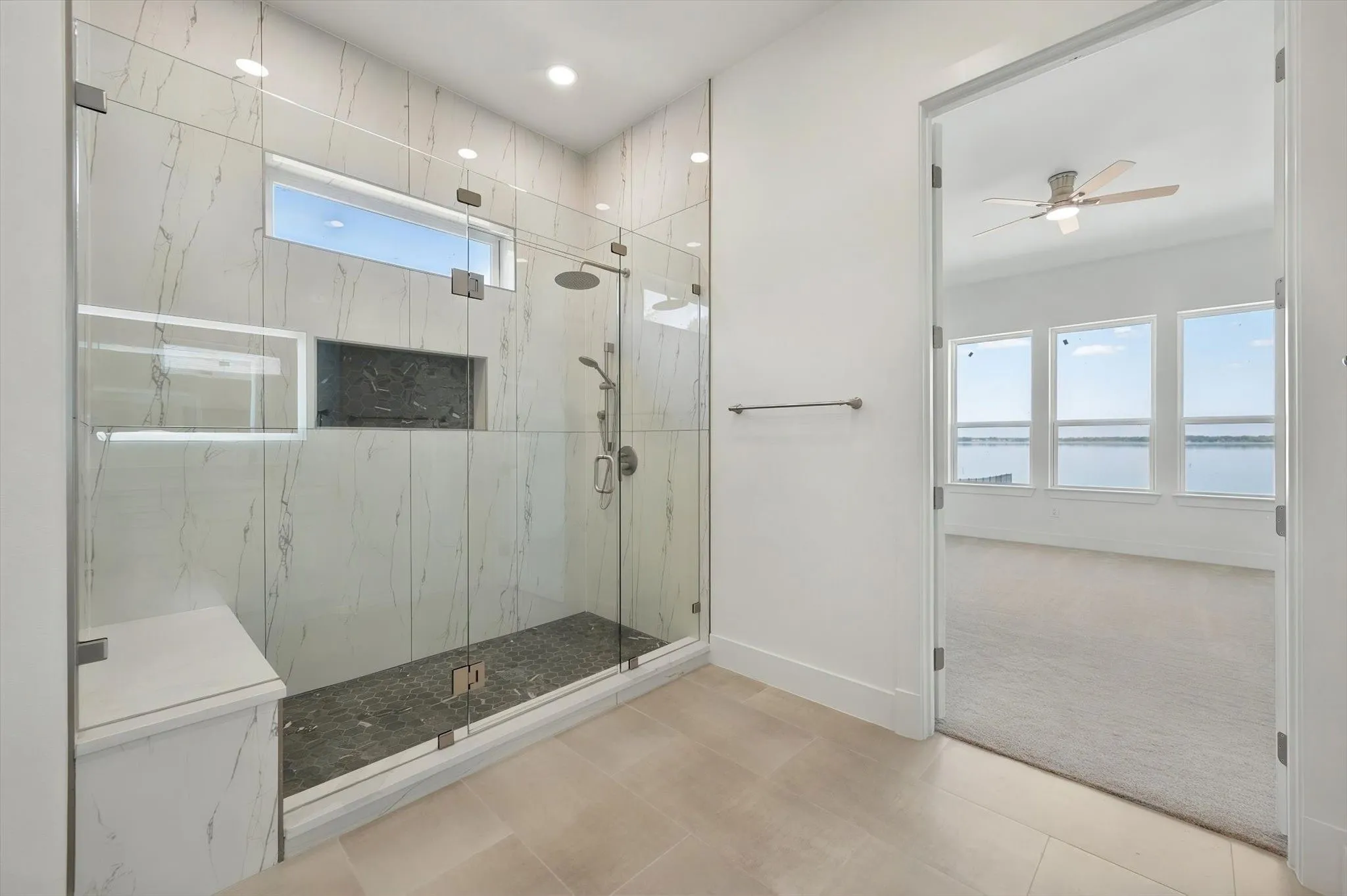 Frameless glass shower view highlighting the seamless view into the light-filled primary bedroom.
