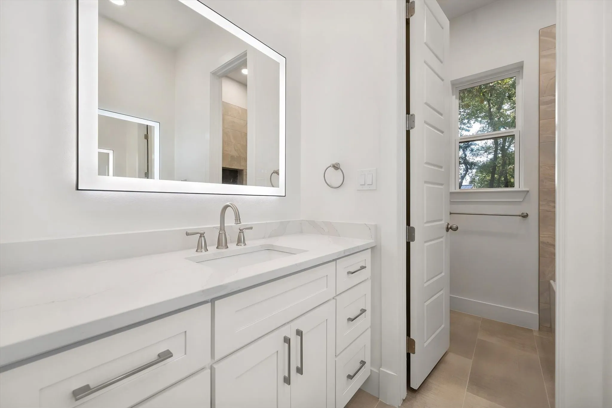 Well-appointed guest bathroom with a white vanity cabinet, LED mirror, and access to a tub/shower combo.
