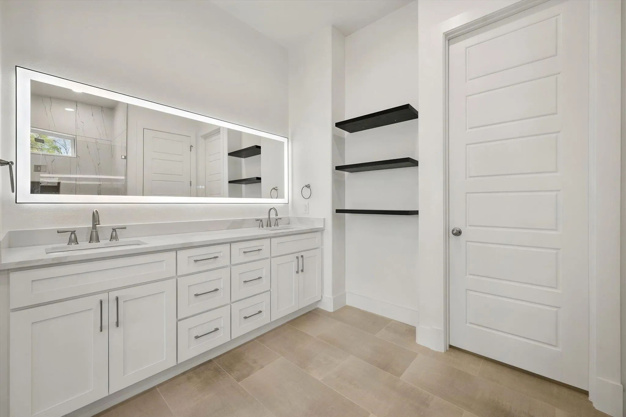 Elegant primary bathroom vanity featuring dual sinks, a large illuminated LED mirror, and custom black floating shelves.