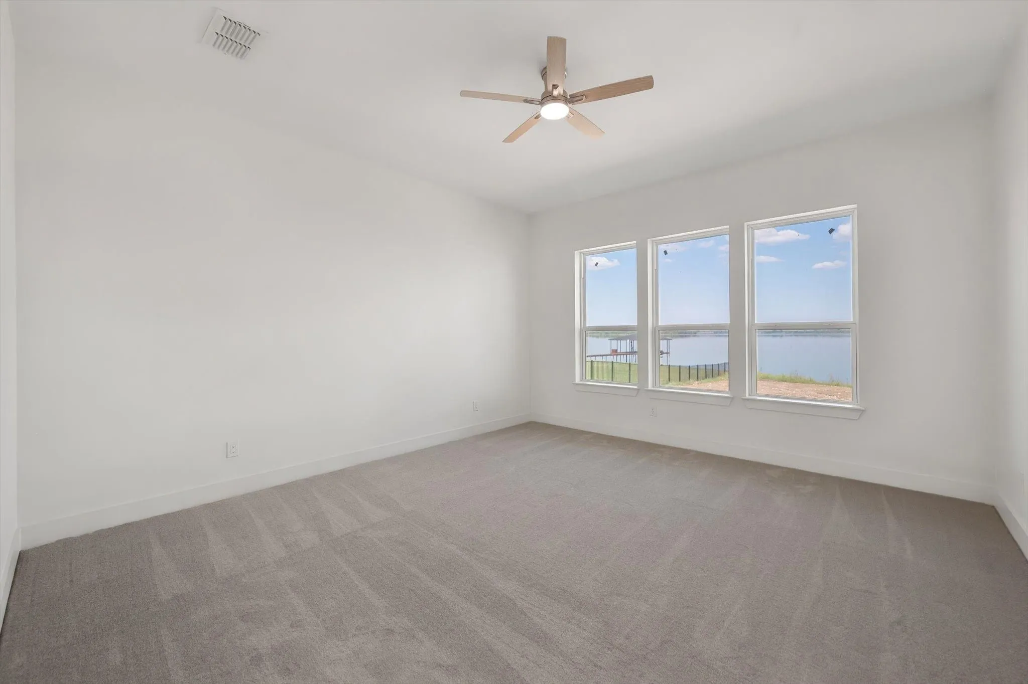 Serene primary bedroom retreat equipped with soft carpet, ceiling fan, and three large windows overlooking Richland Chambers Lake.