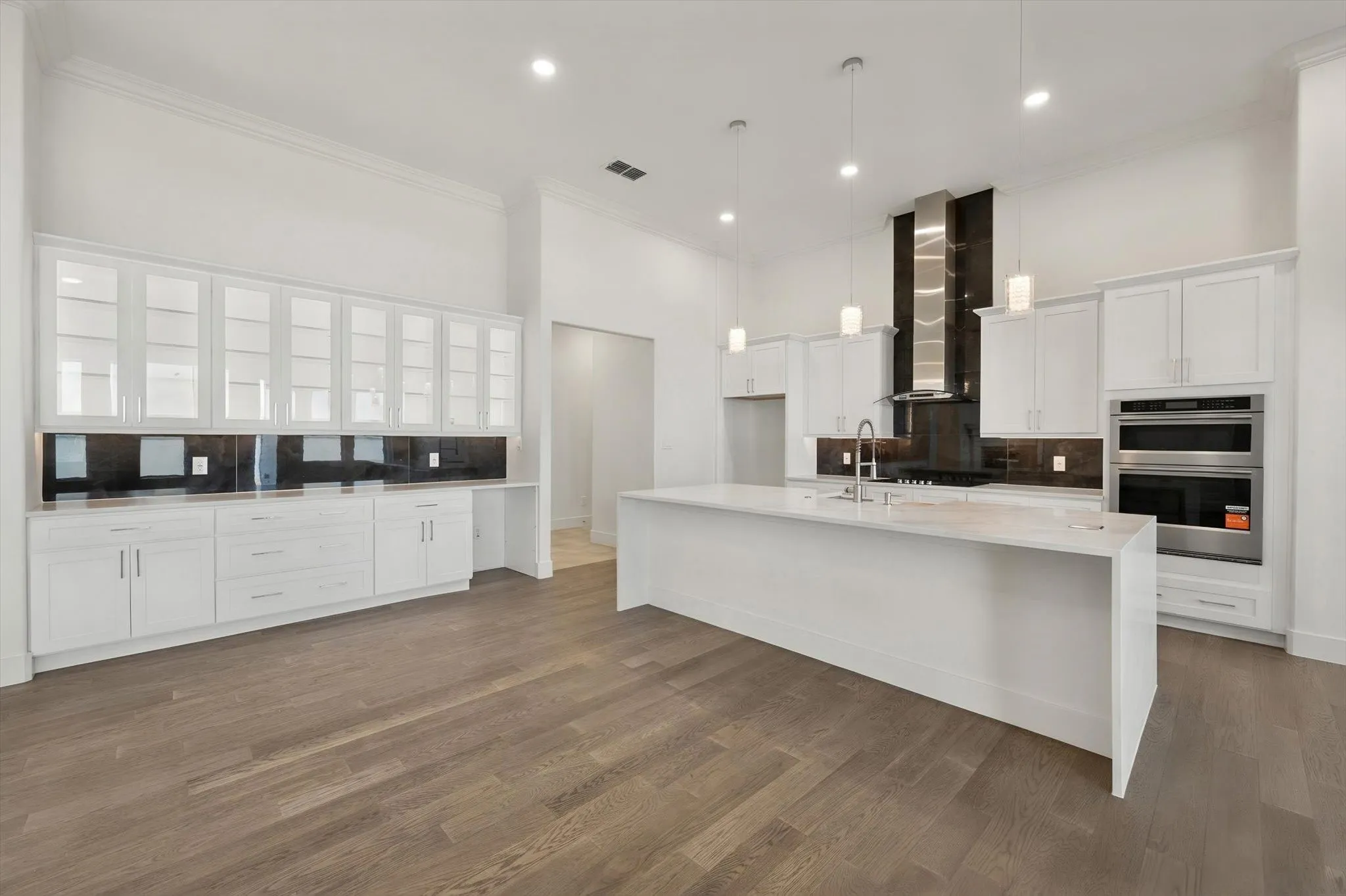 Gourmet kitchen equipped with a large waterfall center island, glass-front lit display cabinets, stainless steel appliances, and dark tile backsplash.