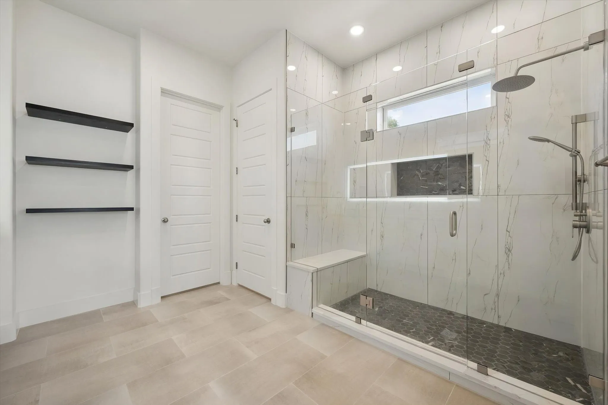 Luxurious primary bathroom featuring a large frameless glass walk-in shower with built-in bench seating and marble-look tile walls.