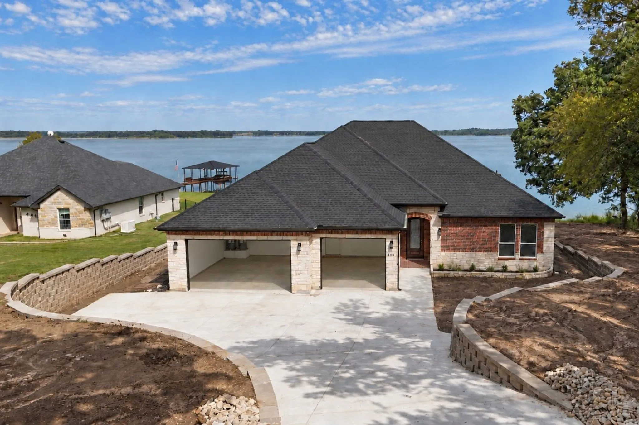 New Build with expected completion date of 10/30/2026. Front elevation of the lakefront home showcasing the spacious three-car garage and retaining wall​​‌​​​​‌​​‌‌​‌‌​​​‌‌​‌​‌​‌​​​‌​​ landscaping.