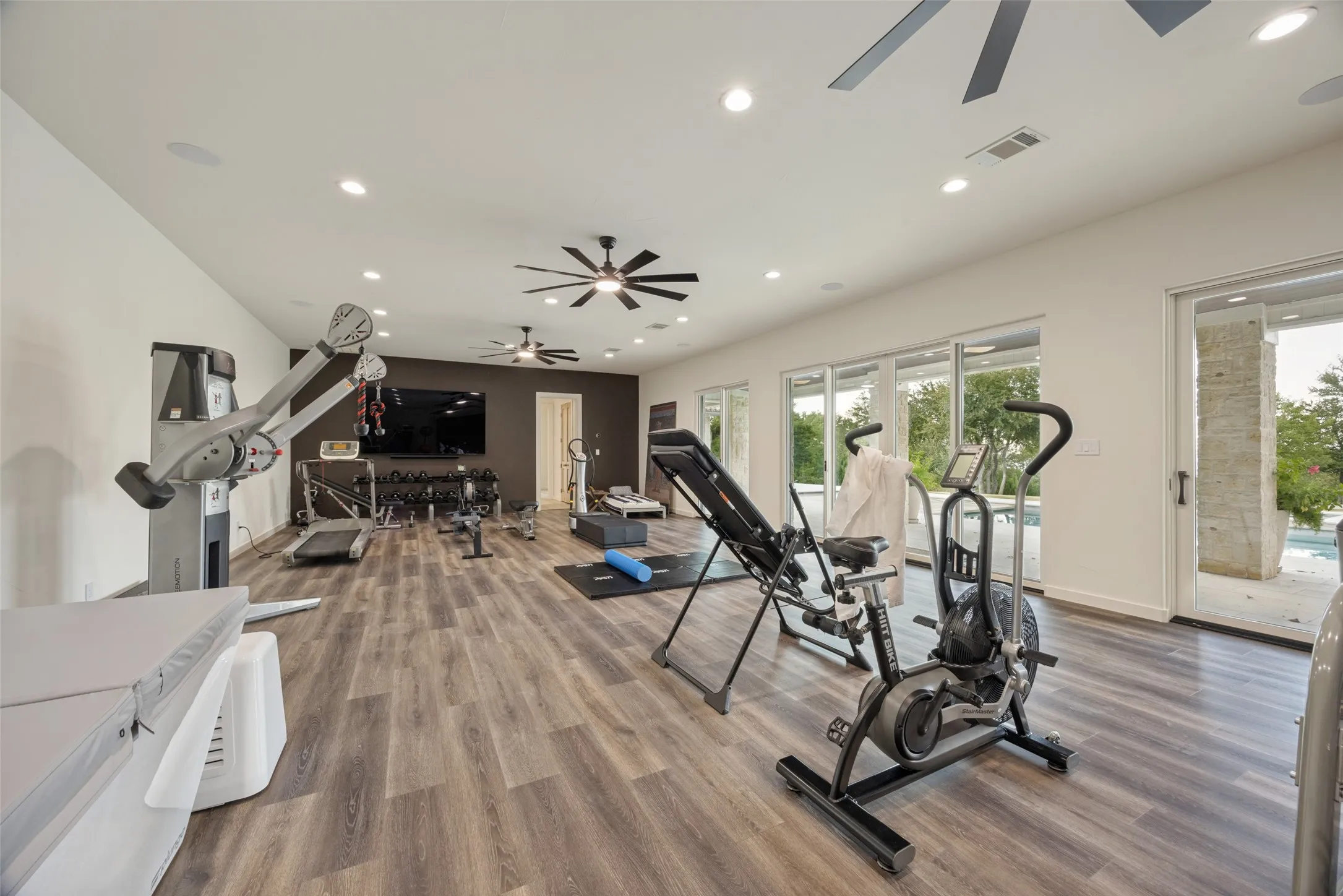 Spacious room featuring wood-finish flooring, recessed lighting, ceiling fans, and a wall of glass doors opening to an outdoor area