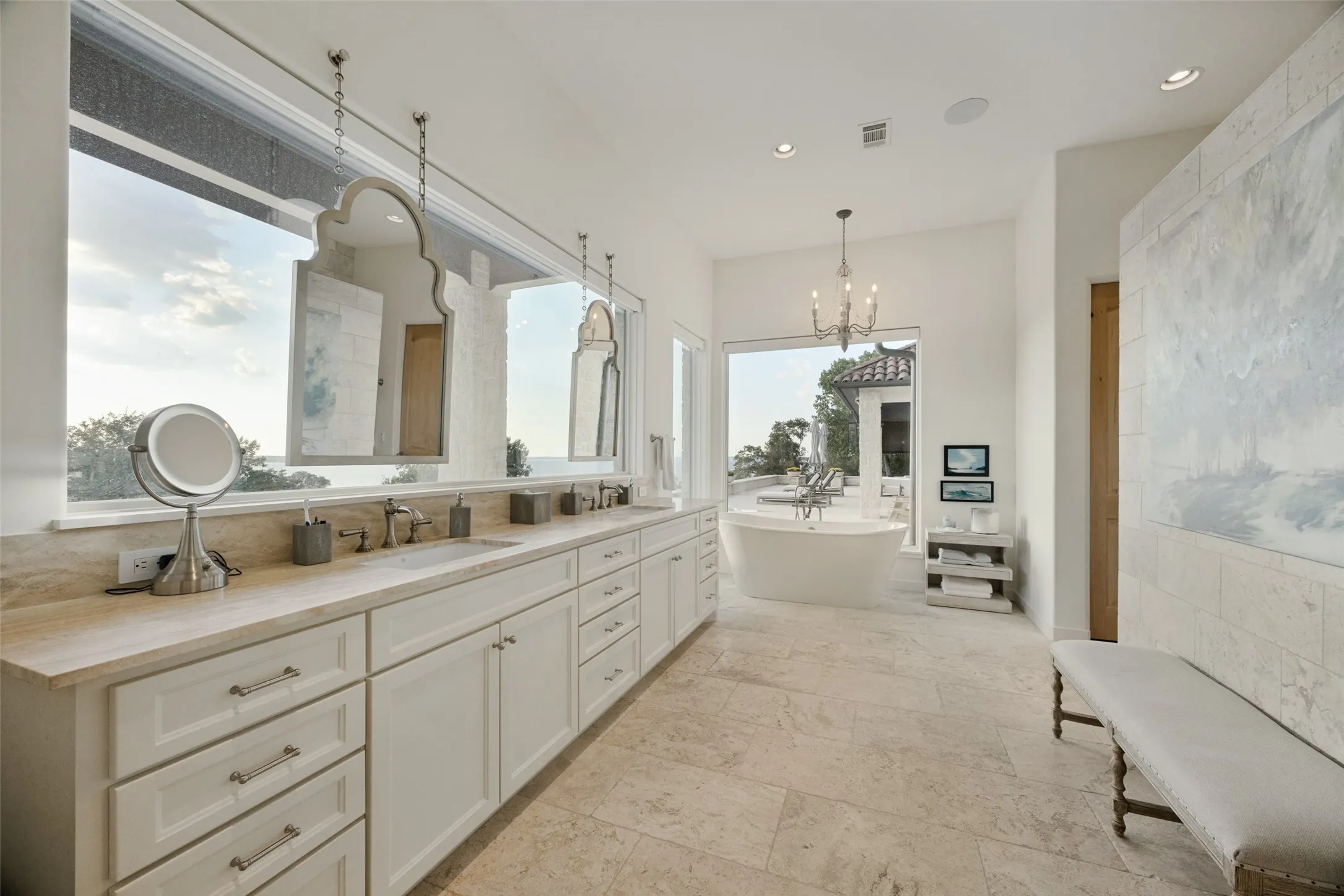 Spacious bathroom featuring a freestanding soaking tub, dual vanity with undermount sinks, light-toned tile flooring, and a large window