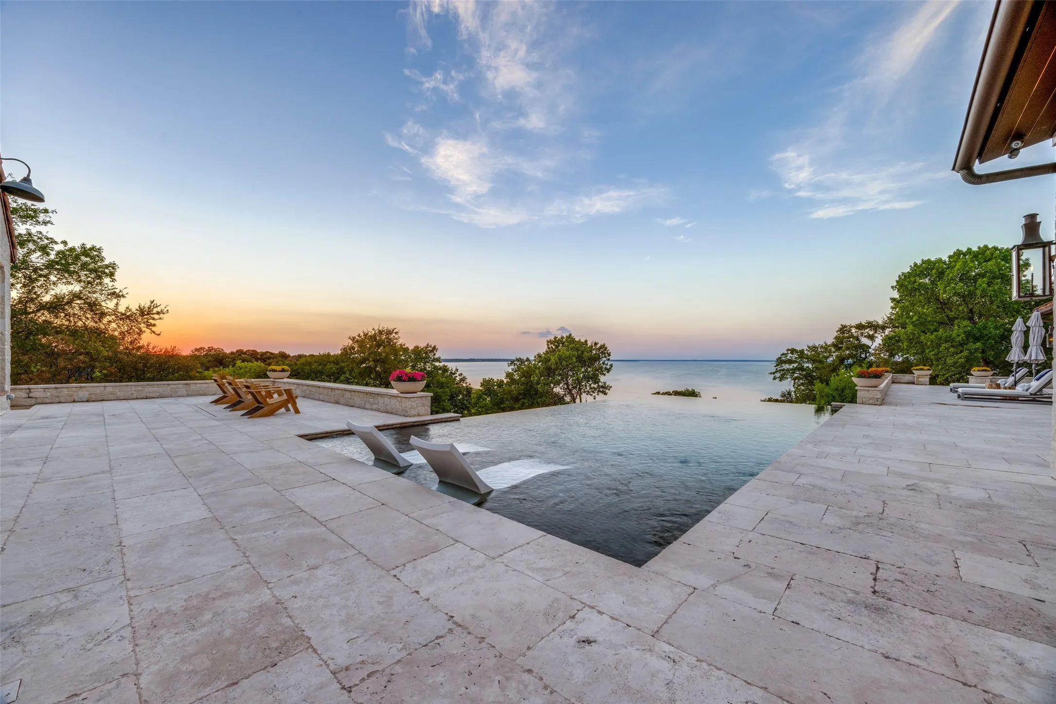 Expansive stone tile patio with an infinity-edge pool, overlooking a substantial body of water