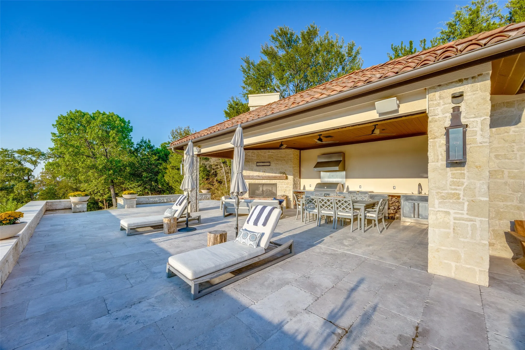 Expansive stone patio featuring a covered outdoor kitchen, built-in fireplace, and stone retaining walls