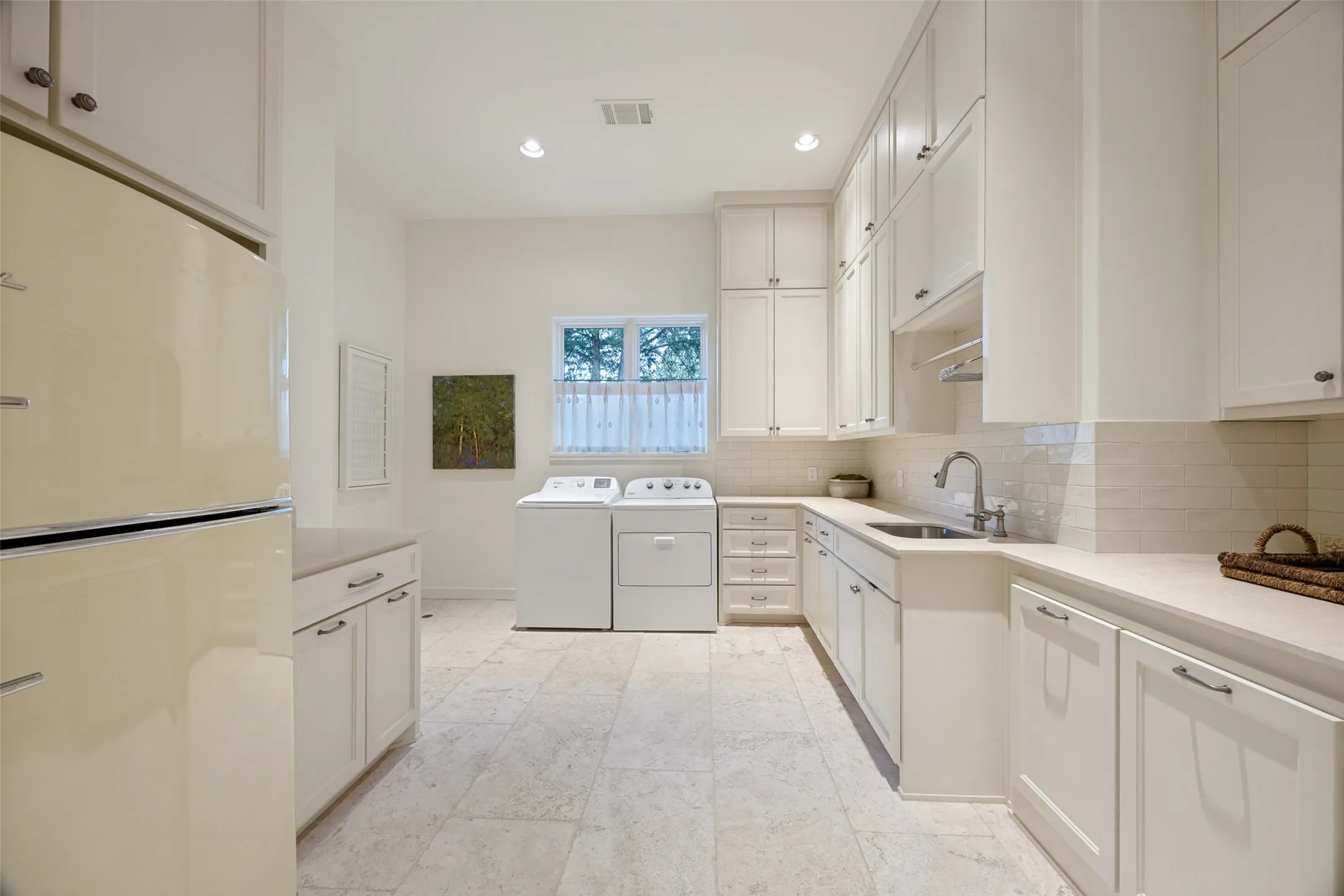 Light-toned tile flooring, extensive white cabinetry, recessed lighting, white subway tile backsplash, and a stainless steel sink with a pull-down faucet
