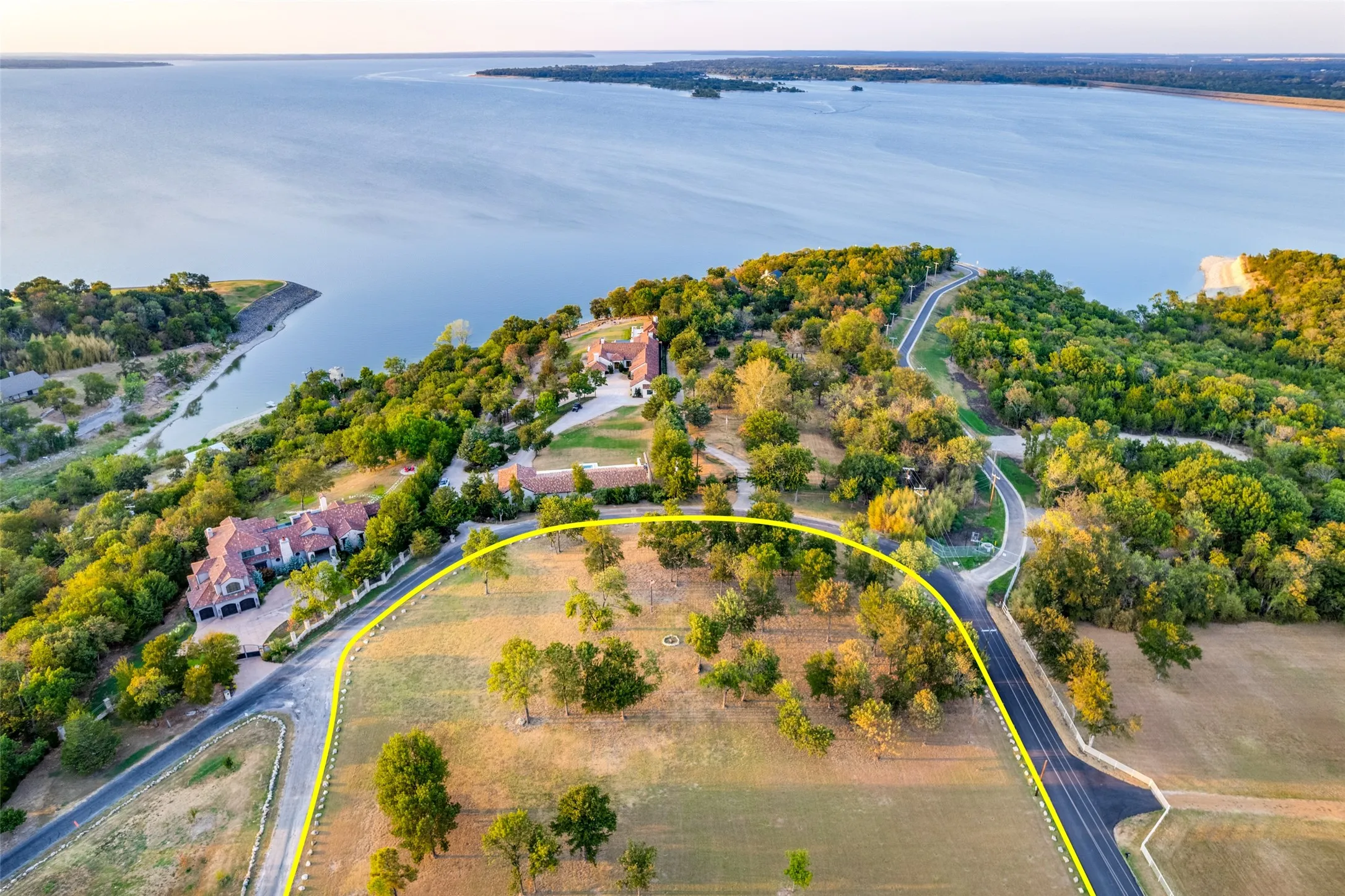 Expansive land parcel with mature trees and paved road frontage