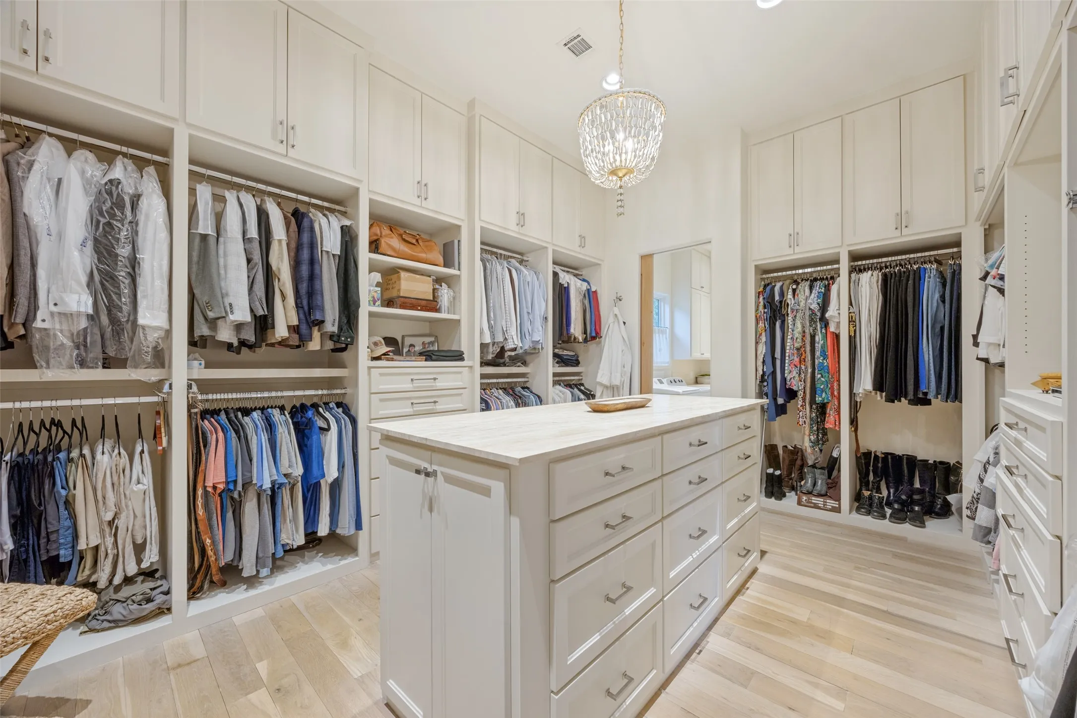 Built-in custom cabinetry, central island with drawer storage, light wood-finish flooring, and a crystal chandelier