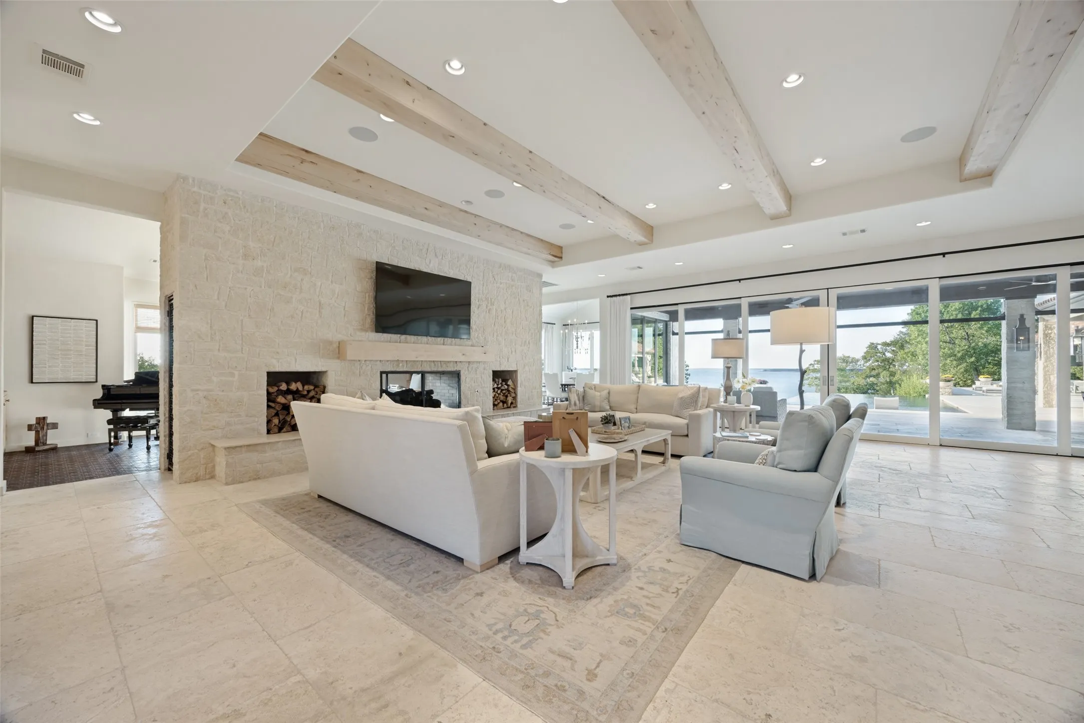 Spacious living area featuring exposed wood beams, recessed lighting, a stone fireplace, large format tile flooring, and expansive glass doors