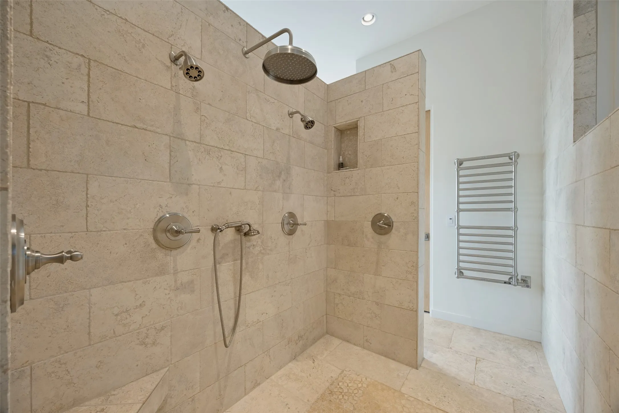Travertine tile shower with multiple shower heads, an integrated niche, and a built-in bench