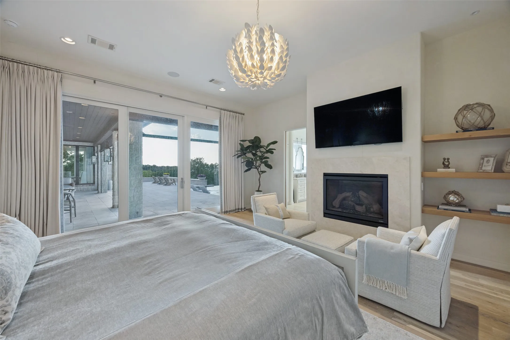 Recessed lighting, a decorative chandelier, a built-in fireplace with a light-toned surround, and floating wood shelves