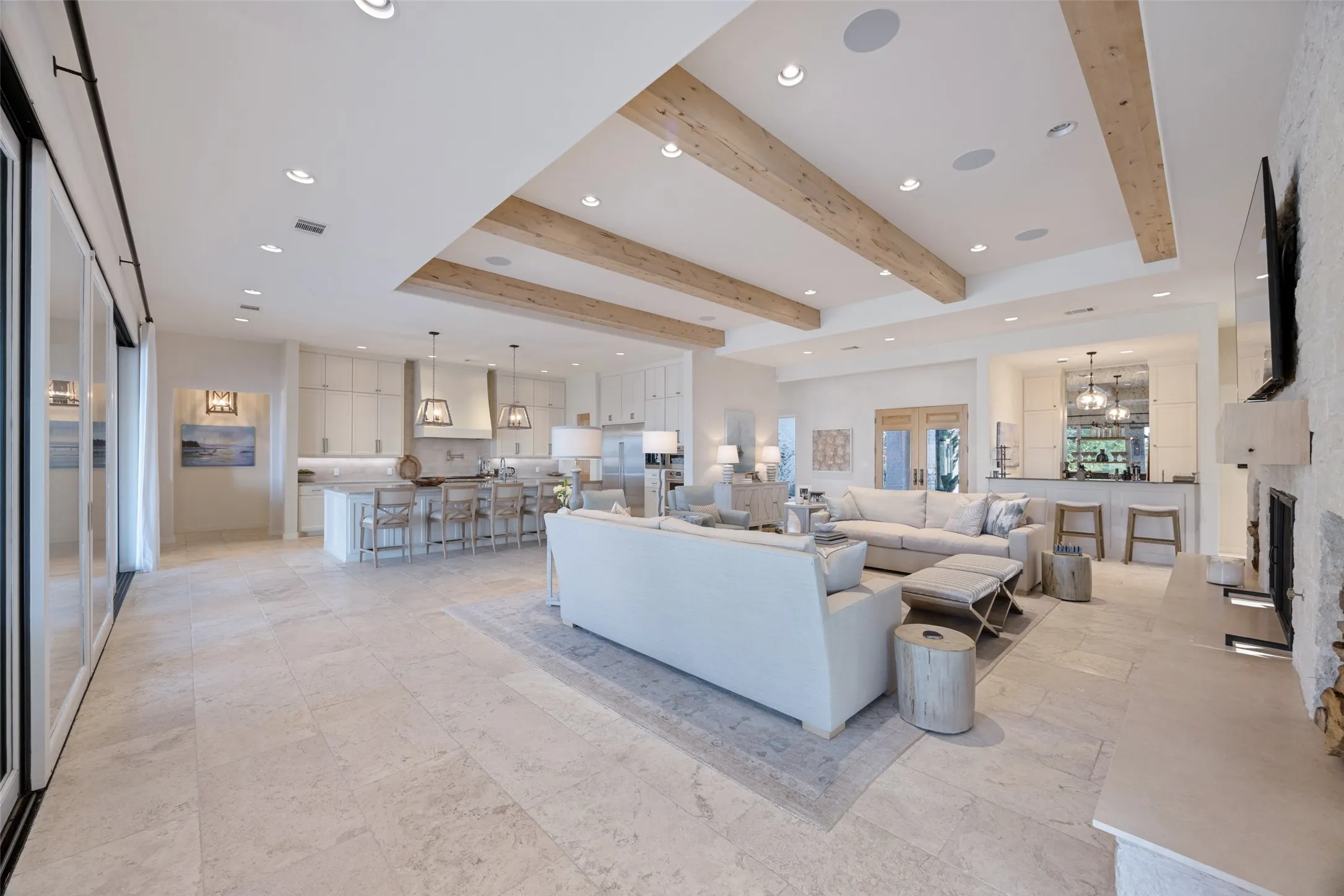Open-concept living space featuring high ceilings with exposed wood beams, recessed lighting, and large format tile flooring