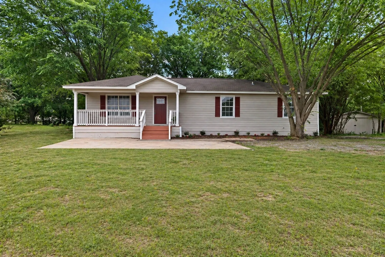 Single-story residence featuring light-colored siding, a covered porch with white railings, a red entry door, and red window shutters