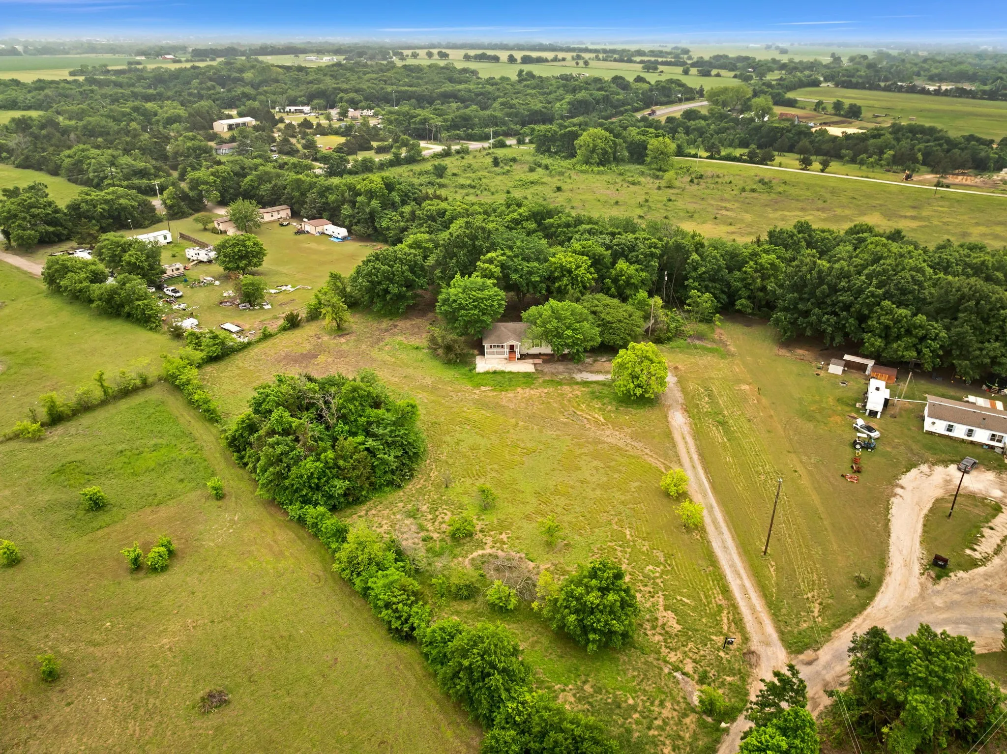 Expansive property featuring verdant fields, a partially paved road, and numerous mature trees
