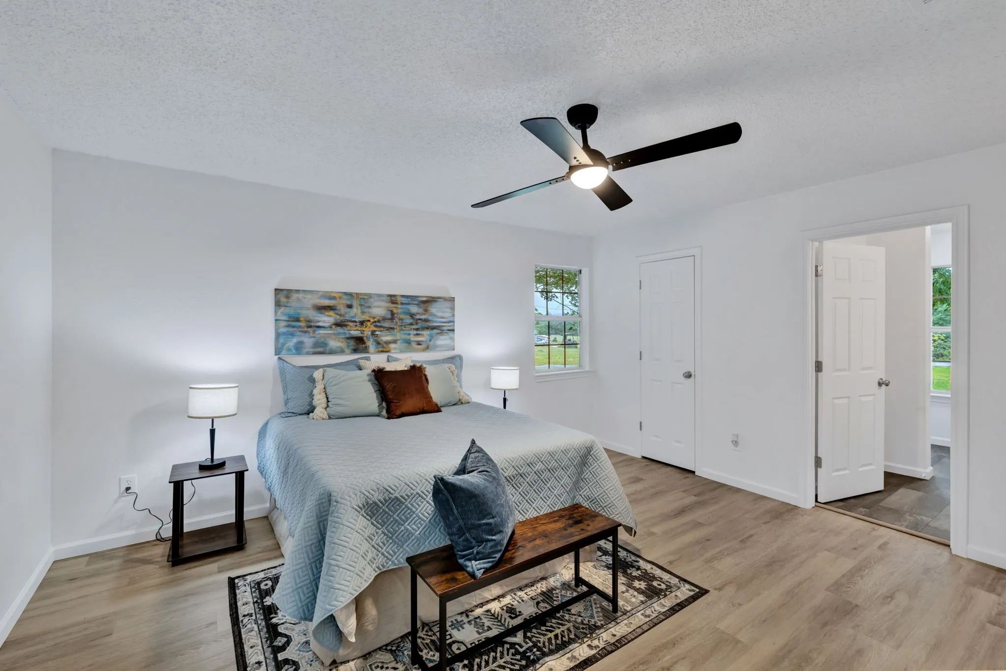 Wood-finish flooring, white walls, black ceiling fan with integrated lighting, and a window with exterior views