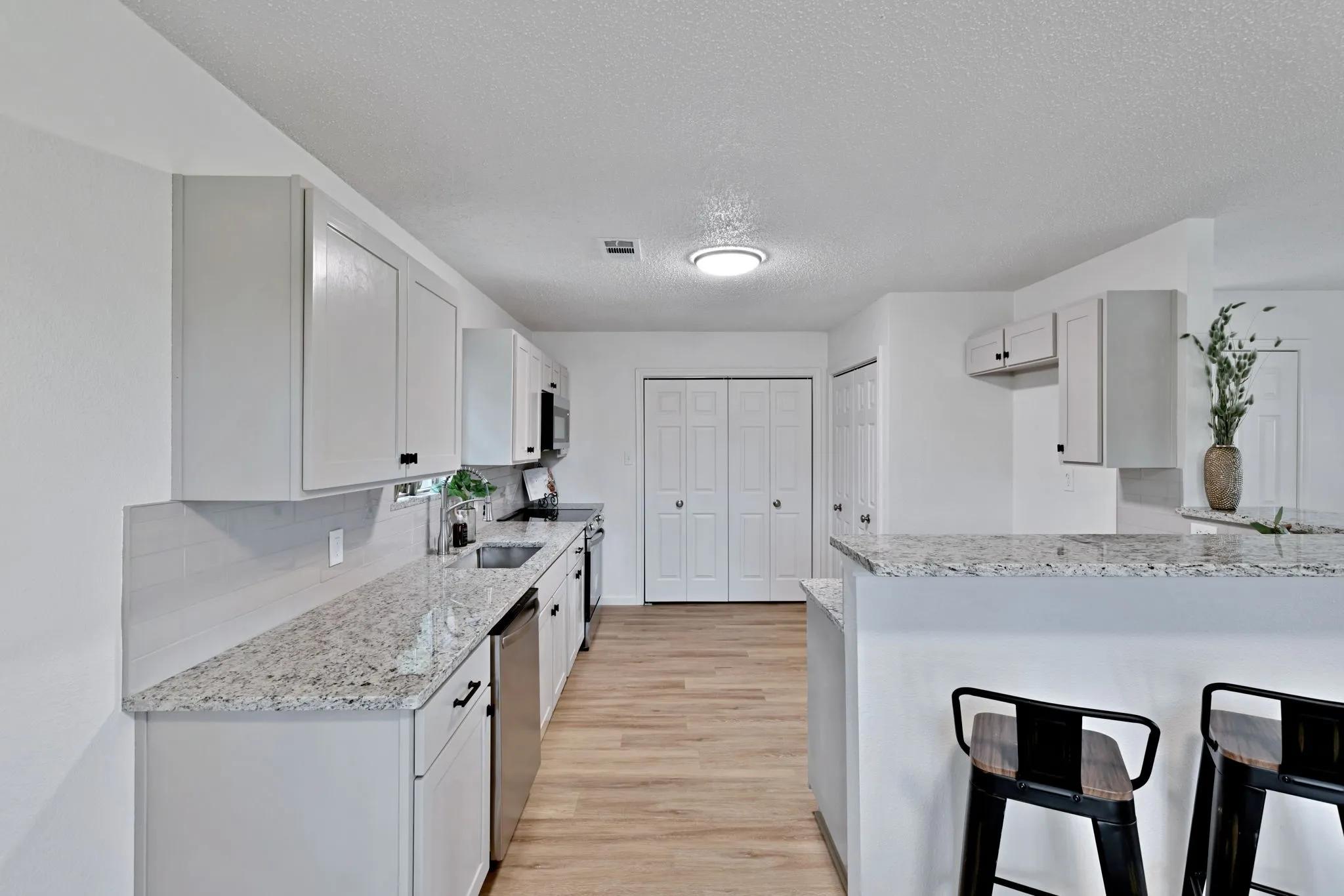 Kitchen featuring white shaker cabinets, light-toned wood-finish flooring, granite countertops, and stainless steel appliances