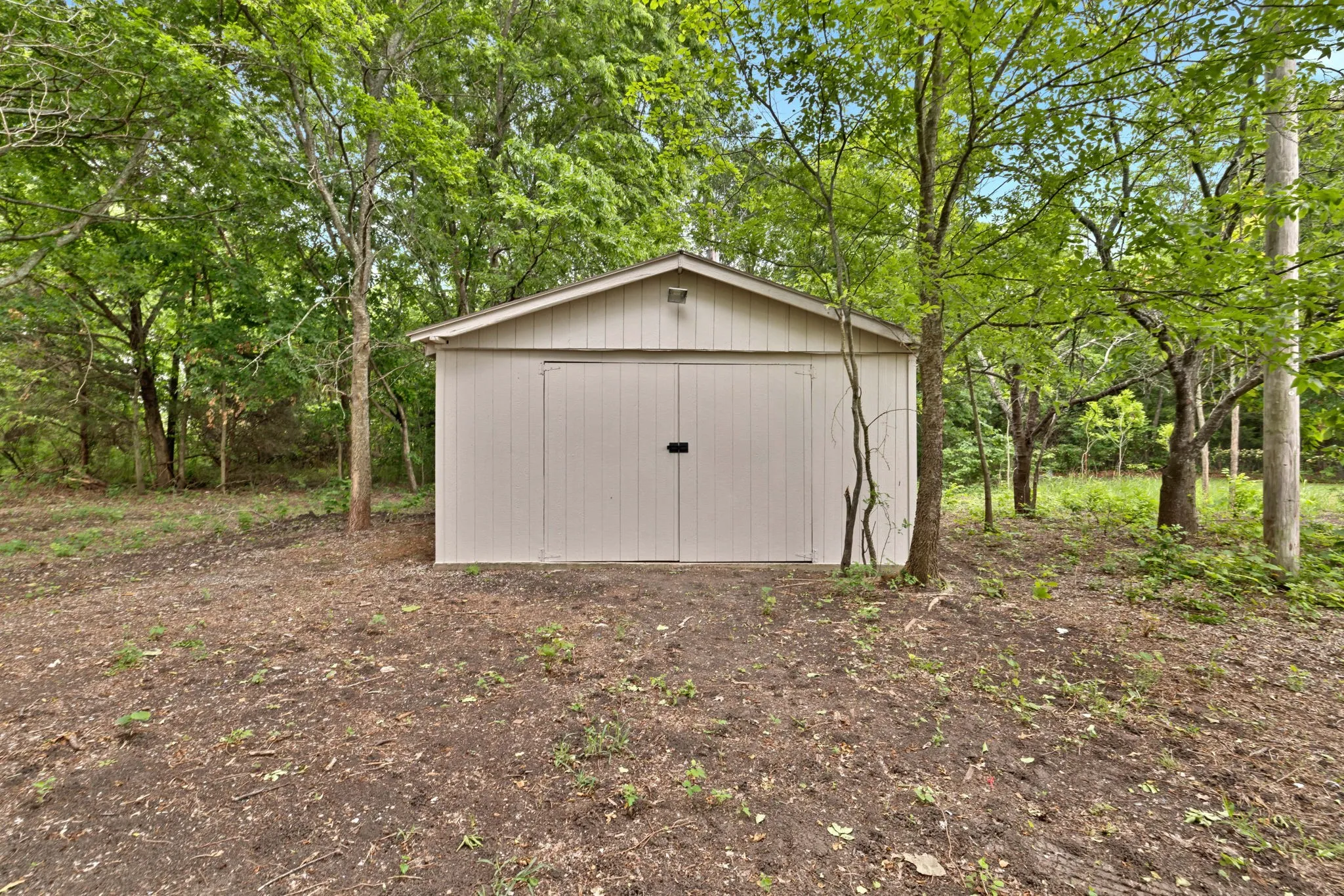 Storage shed with neutral-toned siding, pitched roof, and double entry doors
