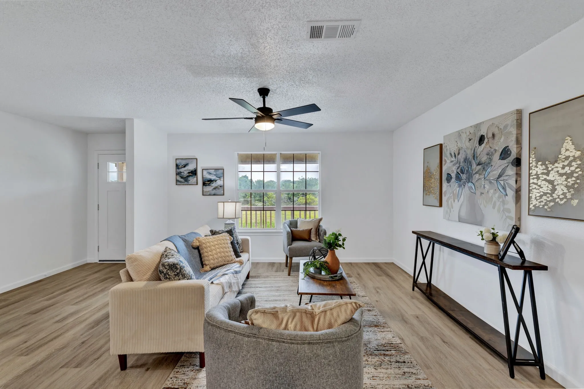 Spacious living area featuring wood-finish flooring, a ceiling fan, and a large window with horizontal muntins
