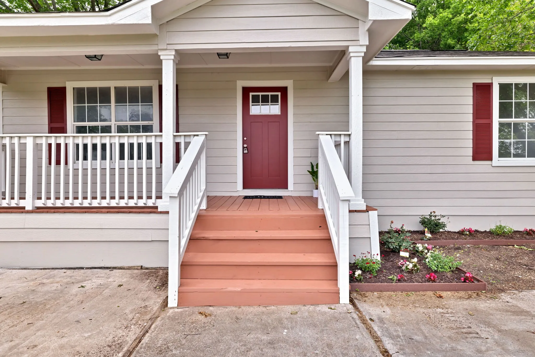 Covered entry porch with white columns and railings, a red front door, and painted wood-finish stairs