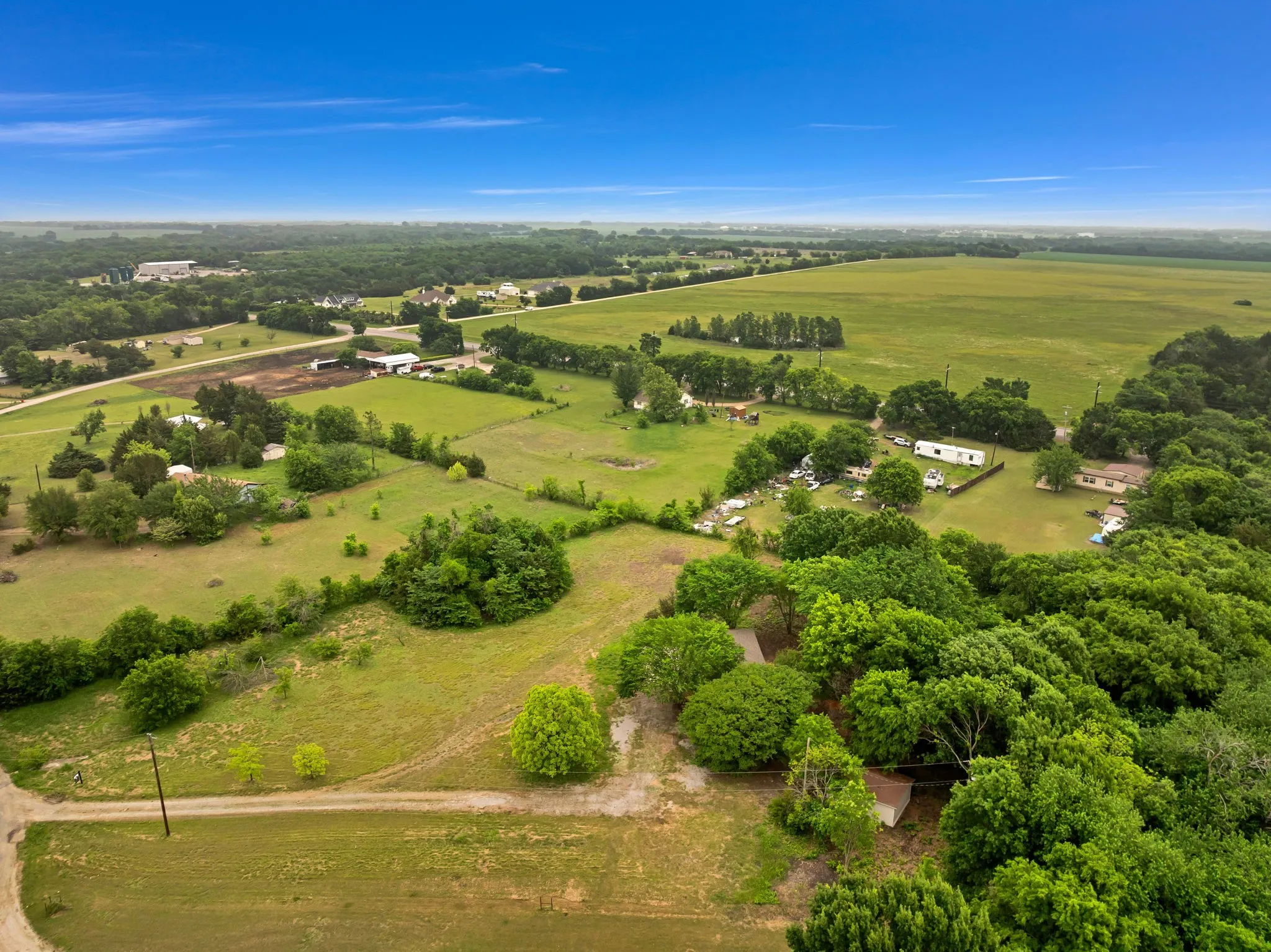 Expansive rural landscape featuring scattered residential structures, mature trees, and agricultural fields