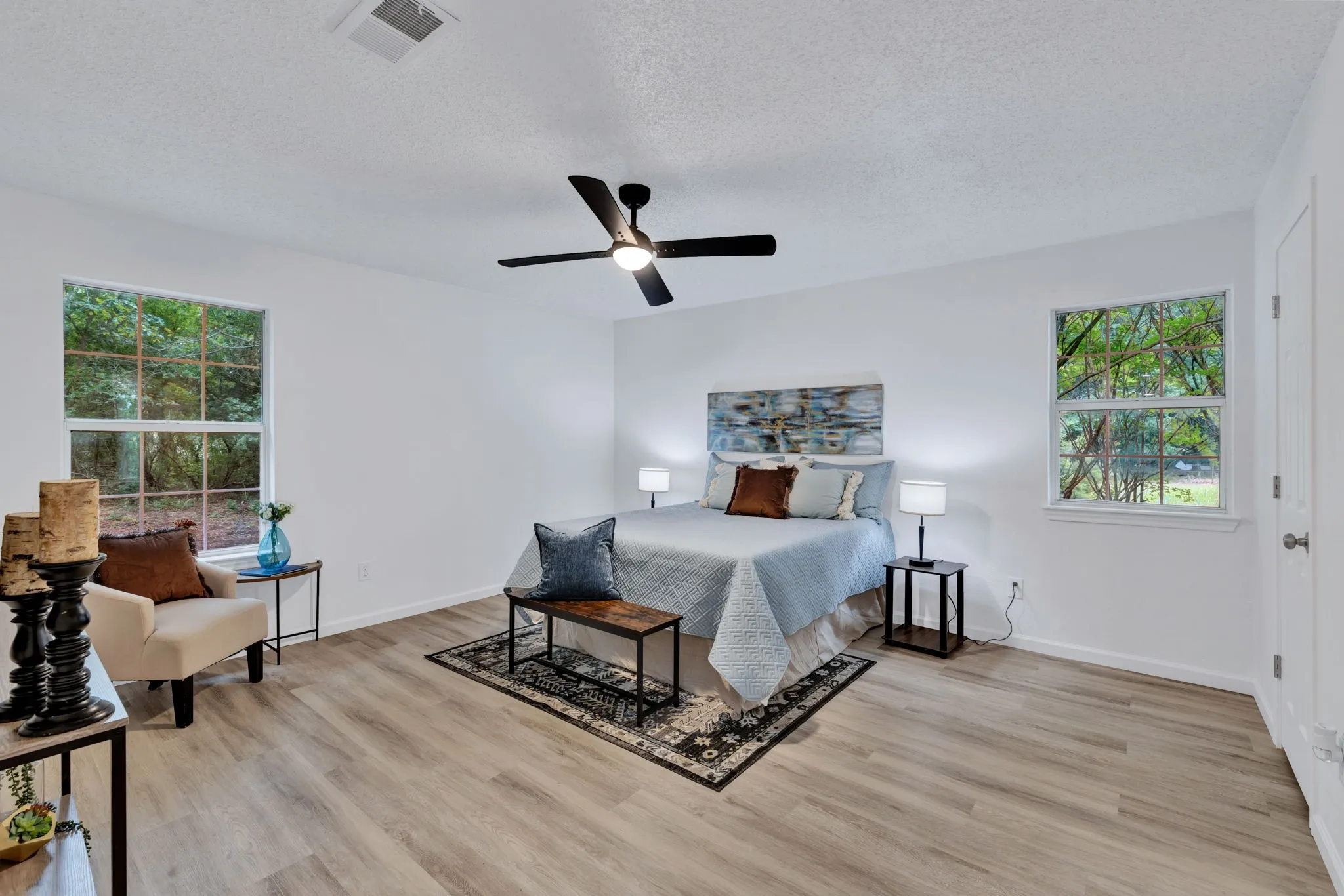 Spacious room featuring wood-finish flooring, white walls, two large windows, and a ceiling fan with integrated lighting
