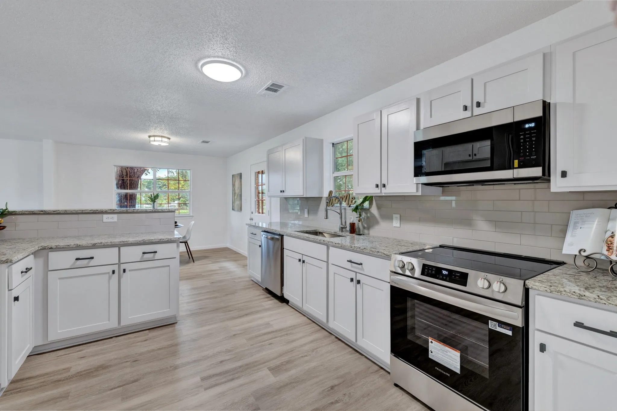 White cabinetry with black hardware, light-toned wood-finish flooring, subway tile backsplash, stainless steel appliances, and light-colored countertops