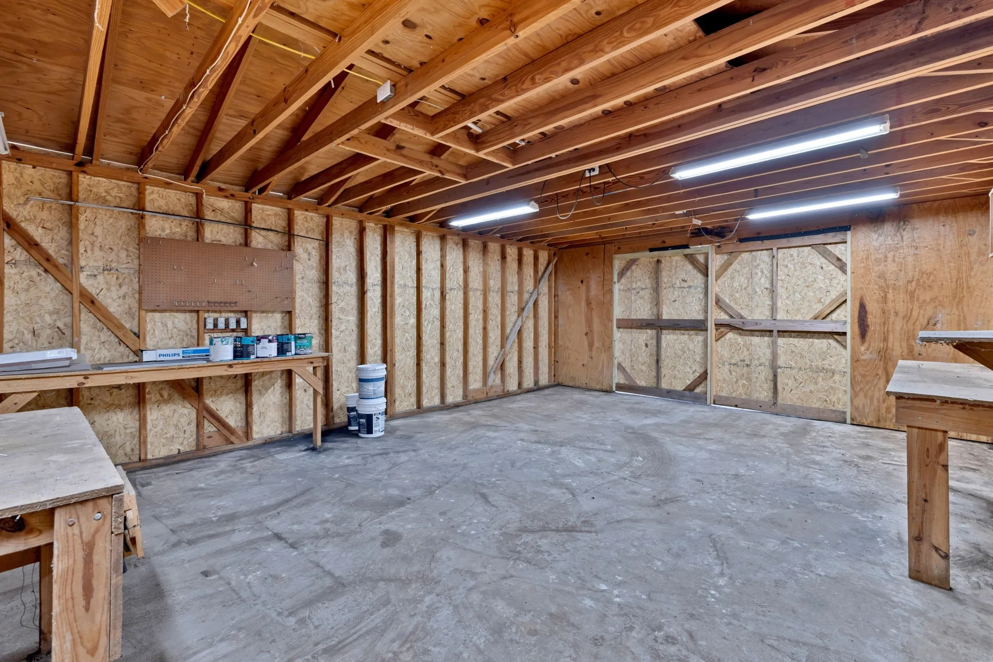 Exposed wood beam ceiling, concrete flooring, built-in workbench, plywood wall paneling, and fluorescent lighting fixtures