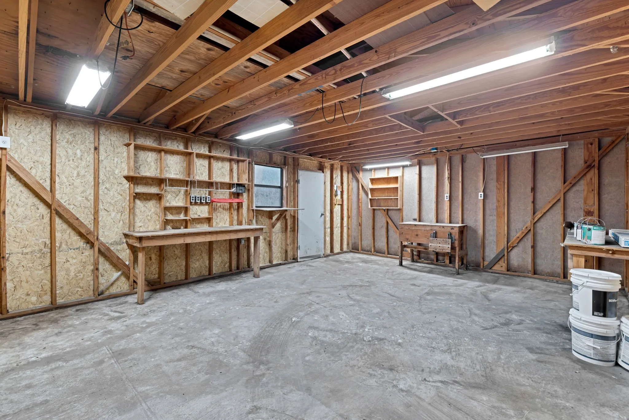 Exposed wood beam ceiling, built-in shelving, concrete flooring, and multiple fluorescent light fixtures