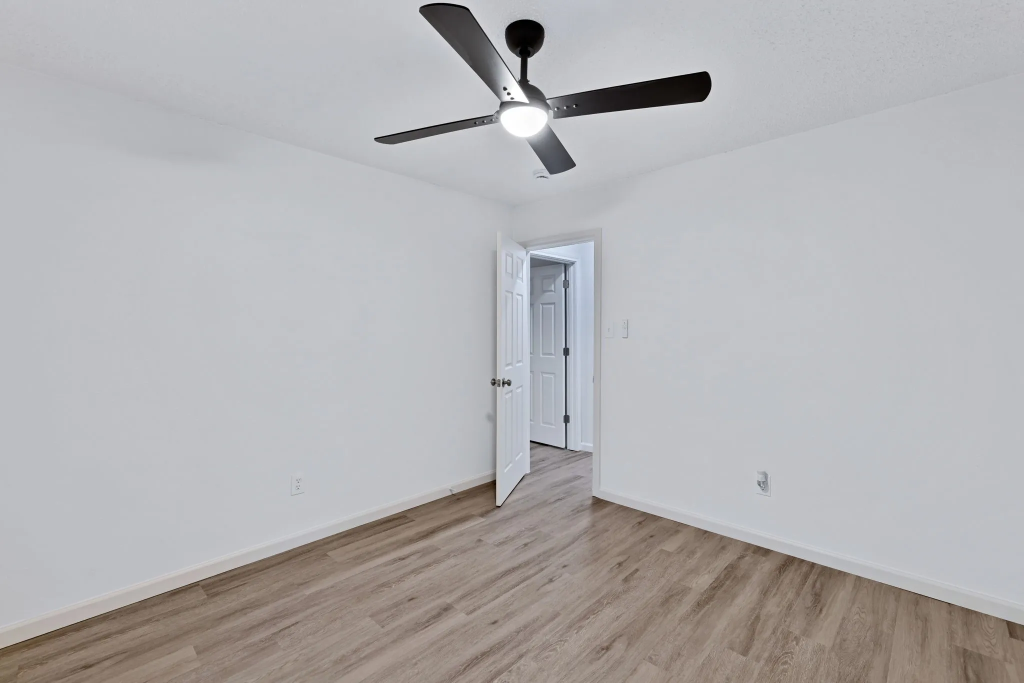 Room featuring wood-finish flooring, white walls, and a ceiling fan with integrated lighting