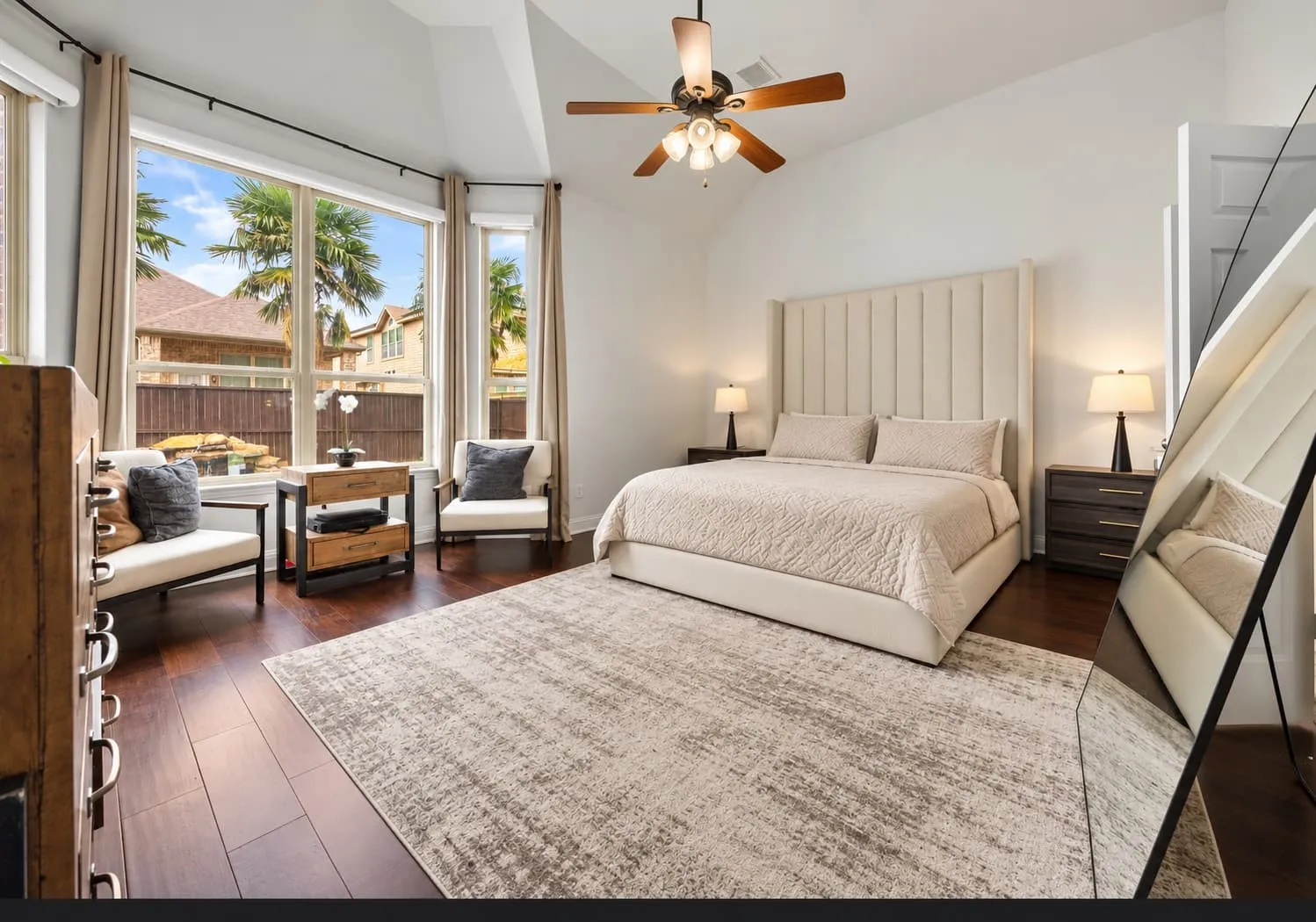 Vaulted ceiling, ceiling fan, wood-finish flooring, multiple large windows, and a panel-style upholstered headboard