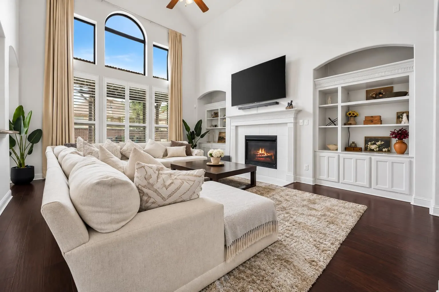 High ceilings with arch-top windows, wood-finish flooring, built-in shelving, and a fireplace with a mantel