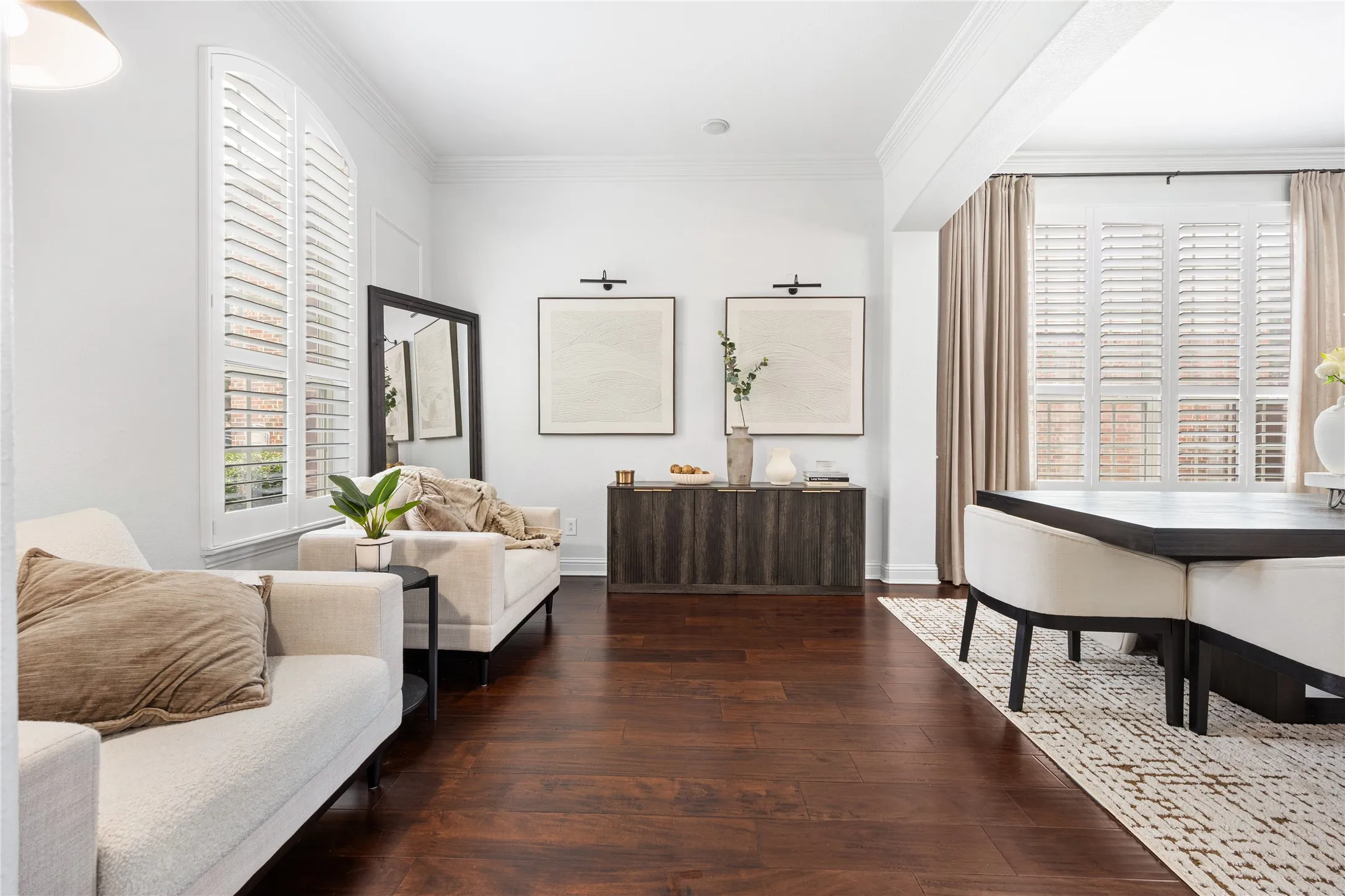 Rich wood-finish flooring, white plantation shutters, built-in wall sconces, and a dark wood-finish credenza