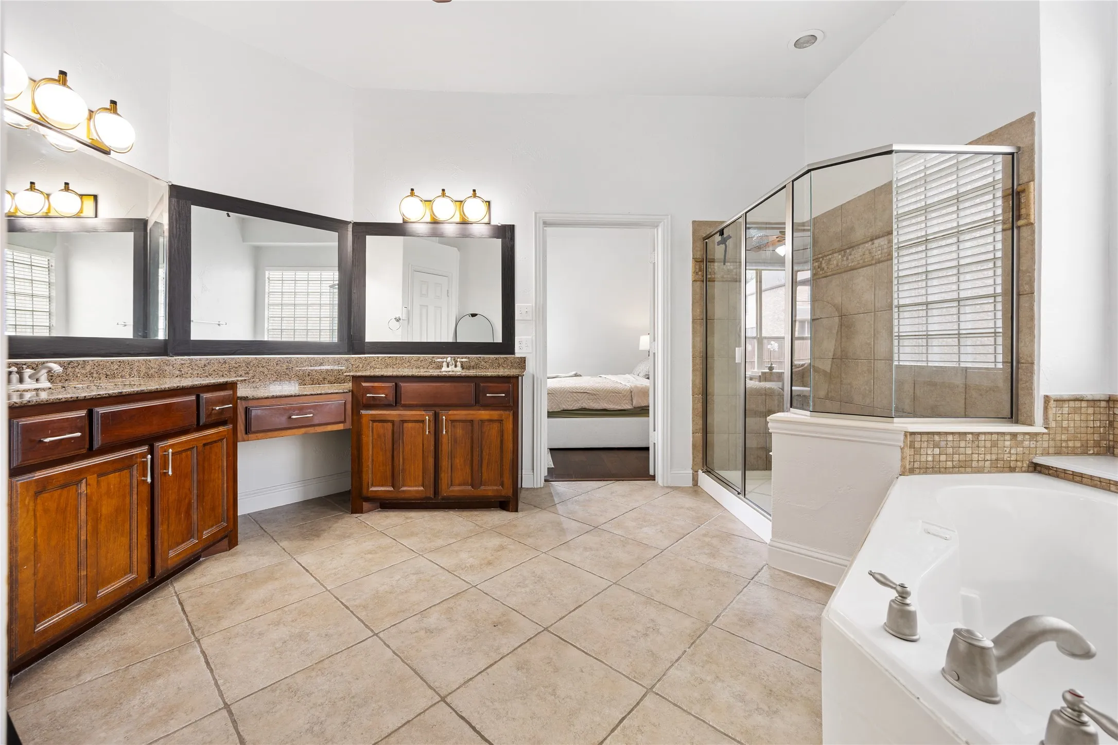 Dual wood-finish vanities with countertop sinks, separate glass-enclosed shower, and a white corner soaking tub