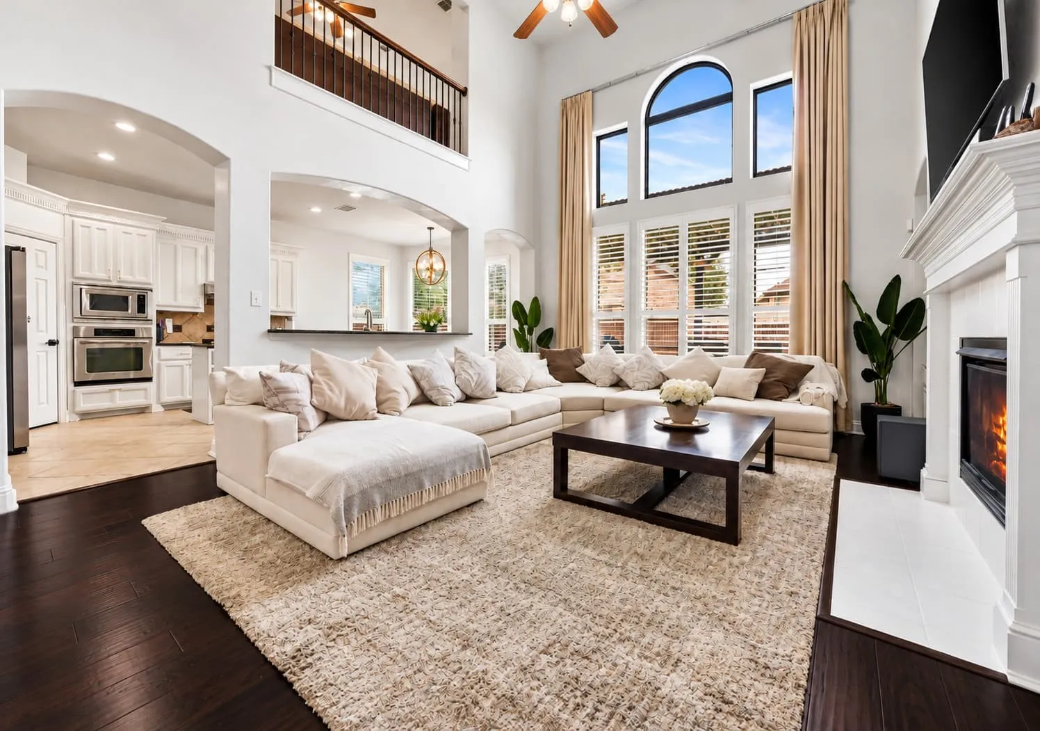 Two-story living area with dark wood-finish flooring, a white mantel fireplace, and a ceiling fan