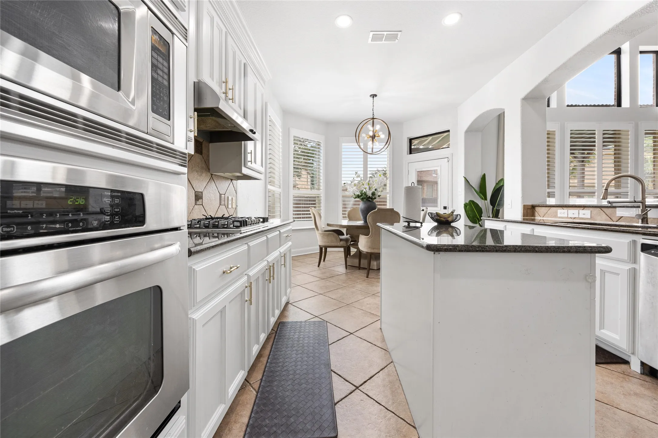 White cabinetry with gold-finish hardware, stainless steel appliances, dark stone countertops, tile flooring, and arched architectural details