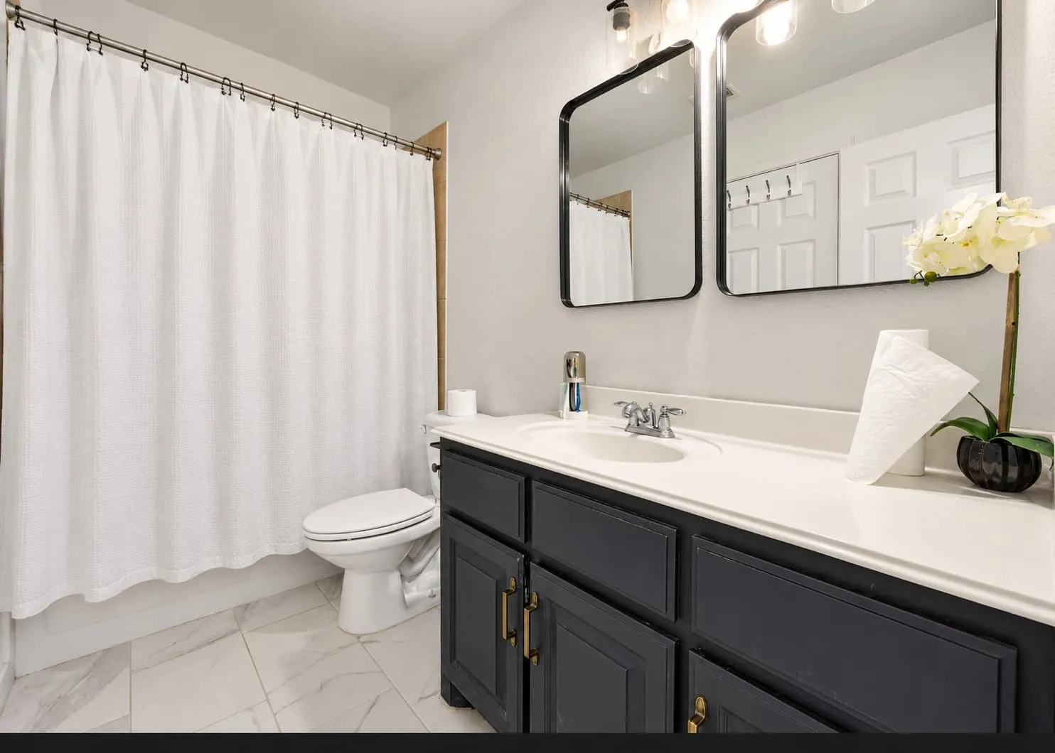 White tile flooring, dual framed mirrors, single vanity with dark cabinetry, integrated sink, and chrome faucet