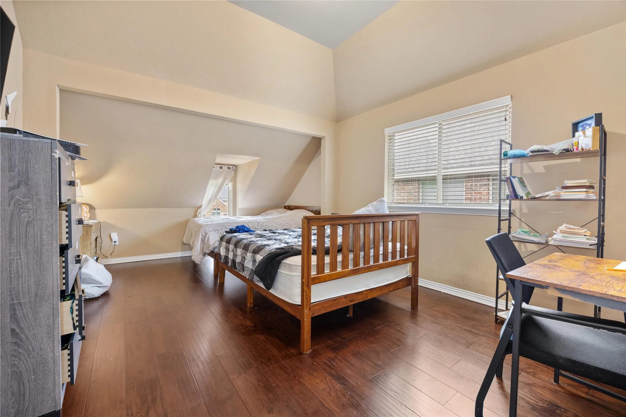 Vaulted ceiling, wood-finish flooring, and multiple windows with blinds