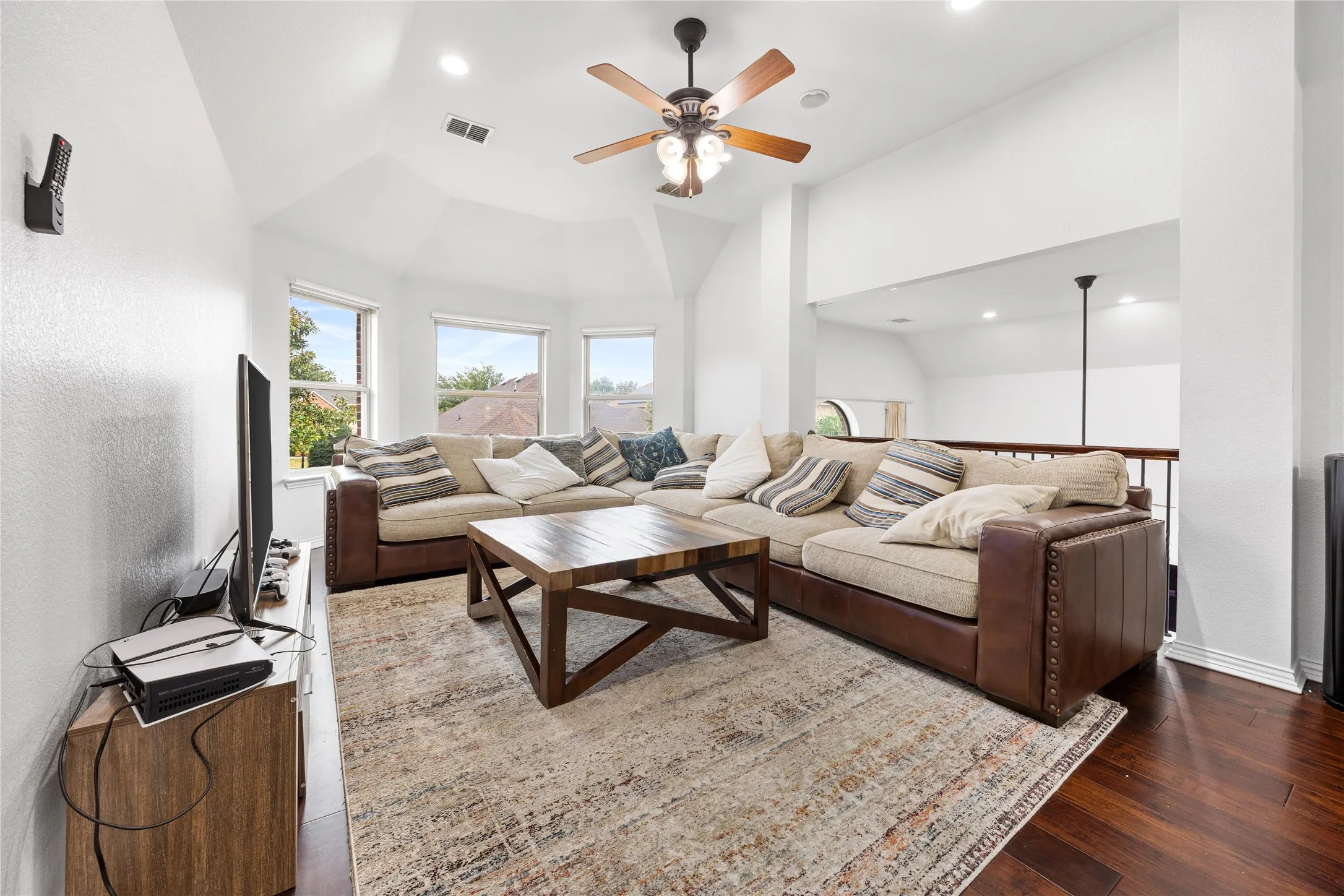 Vaulted ceiling, recessed lighting, ceiling fan, multiple windows, and wood-finish flooring