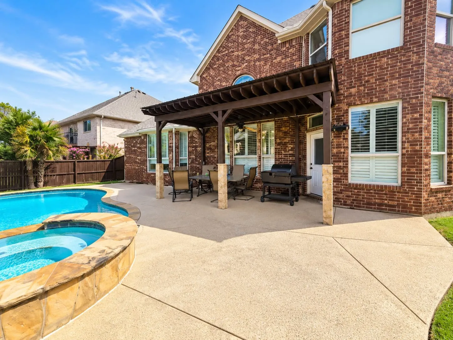 Brick exterior featuring a swimming pool, integrated spa, and an attached wood pergola over a concrete patio